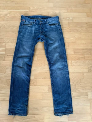 RL Ralph Lauren Jeans - Säljer ett par klassiska blå jeans från Ralph Lauren med rak passform och slitna detaljer vid benslut och bakfickor. Jeansen har fem fickor, knappgylf och är tillverkade i slitstark denim. Perfekta för en avslappnad och trendig look.