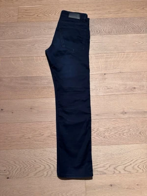 Mörkblå skinny jeans Boss - Snygga mörkblå smala jeans med rak passform och klassisk femficksdesign. Jeansen har en stilren look med diskreta sömmar och en svart patch bak i midjan. Perfekta för dig som gillar en enkel och clean stil. Från Boss. Stl 30/32.