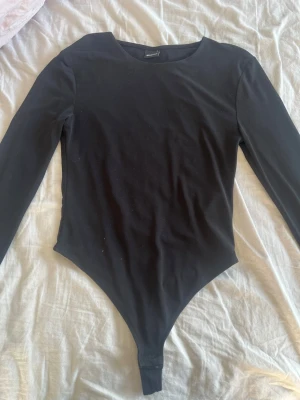 Svart långärmad body från H&M - En enkel och stilren svart body från H&M med långa ärmar och rund halsringning. Tillverkad i stretchigt material som sitter tajt mot kroppen. Perfekt att matcha med jeans eller kjol för en clean look.