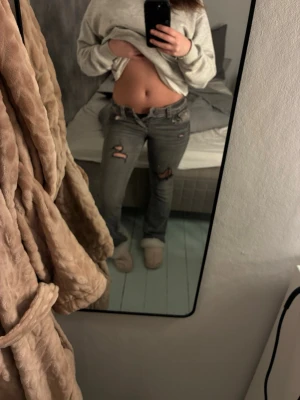 Grå slitna jeans med hål - Säljer ett par grå jeans med slitningar och hål på båda benen från Gina . Jeansen har låg midja och bootcut. Perfekta för en avslappnad och trendig look.