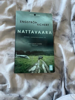 Nattavaara av Engström & Richert - Spännande roman med titeln 'Nattavaara' av Engström & Richert. Omslaget är i gröna och blå toner med motiv av en landsväg, bil och flygplan. Boken är i pocketformat och tryckt på papper. Perfekt för dig som gillar dystopiska berättelser.