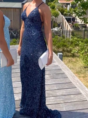 Marinblå balklänning - Säljer min glittriga marinblå balklänning från Dressroom studio. Klänningen har djup v-ringning och öppen rygg. Storlek 36 men klänningen har justerbara axelband samt är stretchig. Endast använd en gång och har inga defekter. Klädpåsen på bild 5 ingår😊Originalpris 4990 kr