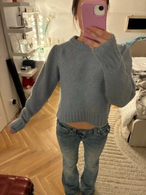 Ljusblå stickad cropped tröja - Mysig ljusblå stickad tröja med croppad passform och rund halsringning. Tröjan har långa ärmar och ribbstickade muddar vid ärmslut och nederkant. Perfekt för lager-på-lager och chill dagar.