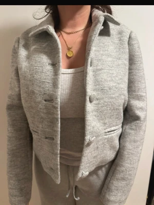 Ljusgrå kort jacka från Object - Kort, ljusgrå jacka från Object i mjukt material med krage och knappar framtill. Jackan har en clean look med två fickor och en rak passform. Perfekt för dig som gillar stilrena och enkla plagg.