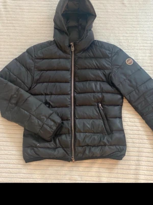 Svart dunjacka från Colmar - Snygg svart dunjacka från Colmar med huva och dragkedja framtill. Jackan har två sidofickor med dragkedja och ett Colmar-märke på ärmen. Perfekt för kalla dagar och riktigt skön att bära. Klassisk quiltad design och stilren look.Artikeln är i bra skick förutom några effekter som syns tydligt på bilden den har hål på båda fickorna längst upp så inget ramlar ur. Den har även ett väldigt väldigt litet hål på framsidan som knappt syns  