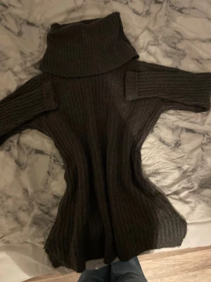 Mörkgrå stickad polotröja - Mysig mörkgrå stickad polotröja med bred polokrage och ribbad struktur. Tröjan har långa ärmar och en något figurnära passform som ger en snygg siluett. Perfekt för kyliga dagar och enkel att matcha med jeans eller kjol.