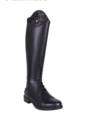 Svart ridstövel med glitterdetalj - Snygg svart ridstövel i läder med snörning framtill och dragkedja bak. Överdelen har en glittrig detalj som ger extra stil. Perfekt för dig som vill sticka ut i stallet eller på tävling. En jättefin ridstövel från QHP strl 38 Wide. Köpta på Bruntes för 1599kr och de är använda ett par gånger men dottern insåg att de är för små. Finns att testa i Munka-ljungby annars skickas mot portokostnad. Se bilder för mått.  Romy Junior Wide - Ridstövlar  Material utvändigt: Läder Material foder: PU syntetma