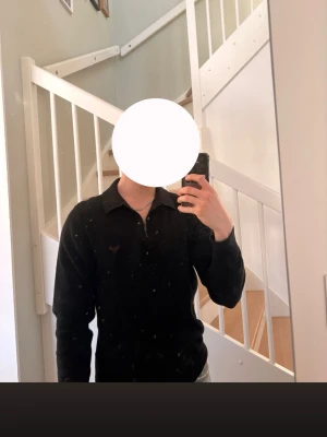 Svart tröja med dragkedja från Threadbare - Säljer en svart långärmad tröja från Threadbare med krage och halv dragkedja framtill. Tröjan har en liten broderad logga på bröstet och är gjord i mjukt material som passar perfekt till en clean och stilren look.