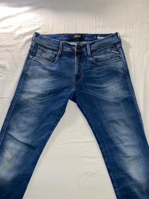 Blå Replay jeans med slitningar - Snygga blå jeans från Replay med klassisk femficksmodell och diskreta slitningar framtill. Jeansen har gul kontrastsöm och Replay-logga vid myntfickan. Materialet är mjukt denim som ger en bekväm passform och cool look.