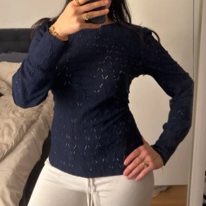 En marinblå tröja från Vila  - Tröjan har dekorativa ihåliga mönster som ger ett elegant uttryck. Den har även resår vid ärmsluten som ger den en extra fin passform på ett stilrent sätt 