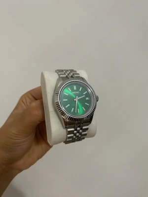 Seiko klocka med grön urtavla - Stilren Seiko klocka med grön urtavla och datumvisning. Klockan har ett klassiskt armband i silverfärgad metall och automatisk urverk som syns genom baksidan. Perfekt accessoar för dig som gillar tidlös design och coola detaljer.