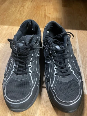 Svarta H&M skor - Snygga svarta  sneakers med vita kontrastdetaljer och CD-logga på sidan. Skorna har meshpaneler för extra ventilation och en chunky sula som ger en modern look. Klassisk snörning och lågt skaft gör dem perfekta för en streetwear-stil.