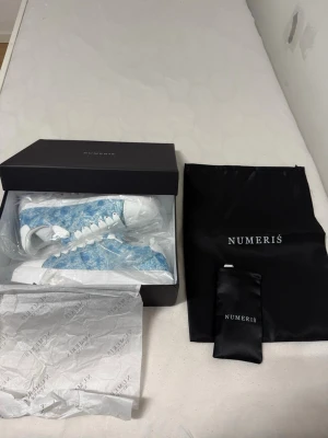 Blå vita sneakers från Numeris - Säljer ett par snygga sneakers från Numeris i blått och vitt med coolt mönster. Skorna har vita snören, vit sula och är tillverkade i tygmaterial. Kommer med originalkartong och dustbag. Perfekta för dig som vill sticka ut med din stil.