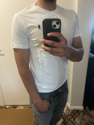Vit t-shirt från Polo Ralph Lauren - Klassisk vit t-shirt från Polo Ralph Lauren med den ikoniska loggan broderad på bröstet. T-shirten har rund hals, korta ärmar och är gjord i mjuk bomull för en skön och stilren look. Perfekt till jeans eller shorts.