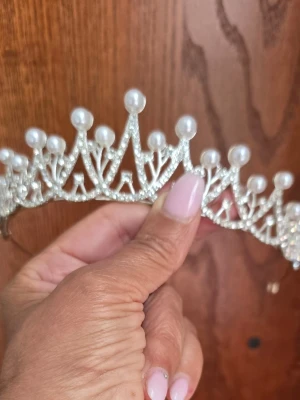Silvrigt diadem med pärlor och strass - Säljer ett glittrande diadem i silverfärg med vita pärlor och strassdetaljer. Diademet har en kronliknande form och ger en lyxig känsla till din look. Perfekt för dig som vill sticka ut och addera lite extra glamour till outfiten.