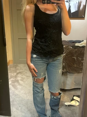 Svart festtopp - Snygg svart linnetopp med strukturerad yta och diskret glittrig effekt. Toppen är ärmlös och har en rundad halsringning. Perfekt att styla med jeans eller kjol för en trendig look. skulle säga passar s-m