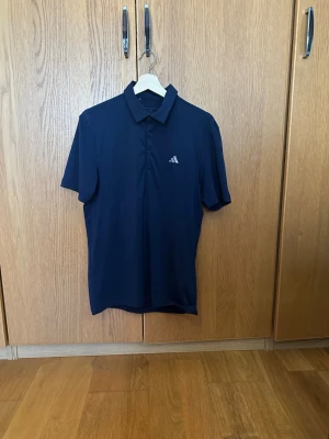 Mörkblå golfpiké från Adidas - Mörkblå piké från Adidas med klassisk krage och knappar framtill som främst är till för golf, men som även funkar i vardagen. Materialet är stretchigt och luftigt. Storleken är S och passar främst för längd runt 173-180. Pikén är använd väldigt lite och inga deffekter finns.