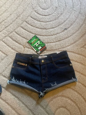 Mörkblå denimshorts från Diesel - Snygga mörkblå denimshorts från Diesel med råa, fransiga kanter och klassisk femficksdesign. Shortsen har låg midja och tydliga kontrastsömmar. Perfekta för sommaren och ger en cool, avslappnad look. Midjemått 38cm o