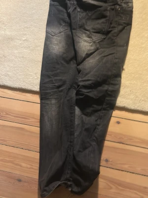 Svarta slitna jeans med tvättade detaljer - Säljer ett par svarta jeans med slitningar och tvättade detaljer. Jeansen har fem fickor, normal midja och raka ben. Materialet är denim och de har en cool, avslappnad look med slitna partier på låret och knät.