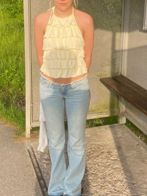 Ljusgul volangig linnetopp - Supersöt ljusgul linnetopp med volanger och halterneck. Toppen är ärmlös och croppad, perfekt för varma dagar. Snygg att styla med jeans eller kjol
