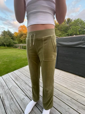 Olivgröna mjukisbyxor Juicy Couture - Snygga äkta olivgröna mjukisbyxor från Juicy Couture i mjuk velour. Byxorna har bred resår i midjan med dragsko, stora fickor fram och bakfickor med lock och silverknappar. Perfekta för en chill och trendig look, jättefina och mysiga på sommarkvällar💕Modellen är 166 cm, byxorna är uppsydda men kan sys ner enkelt💕