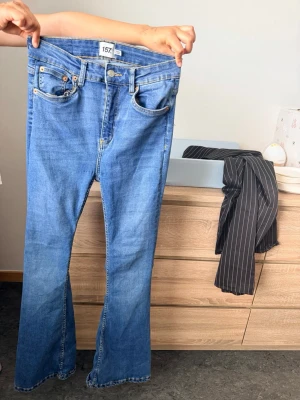 Blå bootcut jeans från 157 - Säljer ett par klassiska blå bootcut jeans från 157. Jeansen har fem fickor, normalhög midja och utsvängda ben. Tillverkade i mjukt denimtyg med snygga sömmar och bälteshällor. Perfekta för en avslappnad och trendig look.