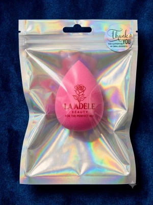 Rosa beautyblender från Laadele - En rosa droppformad beautyblender från Laadele Beauty, perfekt för att applicera foundation och concealer jämnt. Tillverkad i mjukt, flexibelt skum som ger en naturlig finish. Kommer i en holografisk förpackning med elegant rosdetalj på svampen.