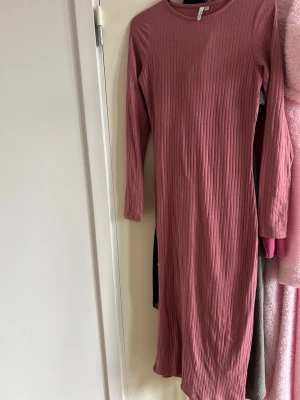 Ribbad långärmad klänning från Only - Mysig ribbad klänning i dammigt rosa från Only. Långärmad modell med rund halsringning och kroppsnära passform. Klänningen är i mjuk bomullsmix och har en enkel, stilren look som passar perfekt till många tillfällen.