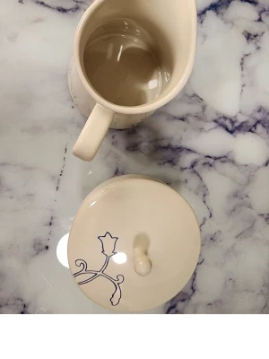 Ikea Krämfärgad mjölk kanna med lock och socker skål blommönster - Säljer en krämfärgad kanna i keramik med tillhörande lock. Kannan har ett stilrent blått blommönster på sidan och locket. Perfekt för servering av sås eller mjölk. Handtaget är robust och designen är enkel men elegant.