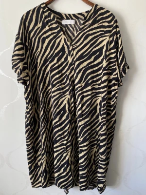 Zebramönstrad loose tunik - Säljer en zebramönstrad klänning från Co'couture i svart och beige. Klänningen har v-ringning, korta ärmar och en loose passform som ger en avslappnad look. Perfekt för dig som gillar djurmönster och vill sticka ut. Den är också perfekt för dig som vill ha något tunt luftigt plag över din baddräkt på sommaren.