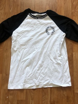 Chrome svartvit långärmad tee - Säljer en svartvit långärmad t-shirt  med kontrasterande svarta ärmar och stora logotryck både fram och bak. Klassisk baseballmodell i mjuk bomull, perfekt för dig som gillar streetwear och vill sticka ut.