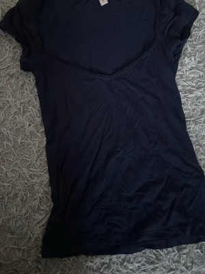 Mörkblå v-ringad topp med spetskant - En enkel mörkblå topp med v-ringning och fin spetskant runt halsen. Kortärmad och i mjukt material som känns skönt mot huden. Perfekt att matcha med jeans eller kjol för en clean look.