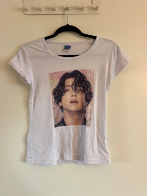 Vit t-shirt med tryck från Fruit of the Loom - Vit t-shirt från Fruit of the Loom med ett färgstarkt tryck av ett porträtt på framsidan. Klassisk rund halsringning och korta ärmar. Tillverkad i mjuk bomull som känns skön mot huden. Perfekt för dig som vill ha en enkel men personlig stil.