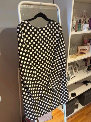Svartvit prickig långärmad klänning - Säljer en svart klänning med stora vita prickar och långa ärmar. Klänningen har en rak passform och är i kort modell. Perfekt för dig som gillar retrovibbar och ett lekfullt mönster.
