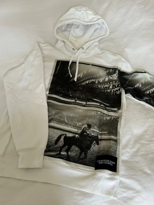 Vit hoodie Calvin Klein x Andy Warhol - Säljer en vit hoodie från Calvin Klein i samarbete med Andy Warhol. Framsidan har ett stort svartvitt fototryck med motiv.