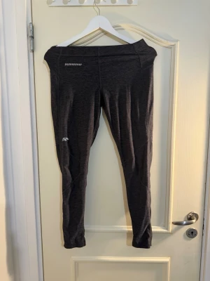 Mörkgrå sportleggings från SOC - Snygga mörkgrå sportleggings från SOC med svarta paneler längs benen. De har en smal passform och är tillverkade i ett stretchigt funktionsmaterial som andas. Perfekta för träning eller chill dagar. Diskreta loggor framtill och baktill.