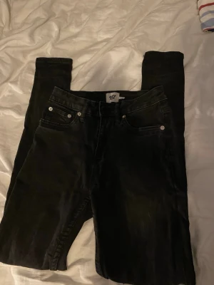 Svarta skinny jeans från 157 - Säljer ett par svarta skinny jeans från 157 med klassisk femficksdesign och smal passform. Jeansen har silverfärgade nitar och knapp, samt bälteshällor i midjan. Perfekta för dig som gillar en enkel och stilren look.