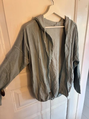 Ljusgrå hoodie med huva - En oversized ljusgrå hoodie med huva och dragsko. Modellen är öppen framtill utan dragkedja eller knappar och har långa ärmar. Tillverkad i mjukt bomullsliknande material som känns skönt mot huden. Perfekt för en avslappnad och chill stil.