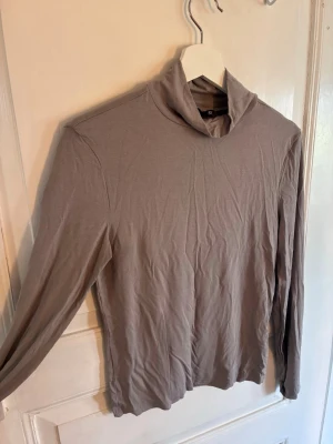 Beige långärmad polotröja Lager 157 - Säljer en beige långärmad polotröja från 157. Tröjan är i mjukt och tunt material, har en lös polokrage och enkel, stilren design utan tryck eller mönster. Perfekt att styla lager på lager eller bära som den är.