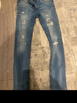 Ljusblå slitna skinny jeans - Säljer ett par ljusblå skinny jeans med flera slitningar och hål på både fram- och baksida av benen. Jeansen har klassisk femficksmodell och är tillverkade i stretchigt denimtyg för en bekväm passform. Perfekta för en avslappnad och trendig look.