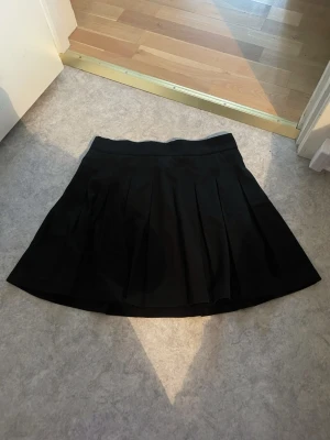 Svart plisserad kjol från Stradivarius - Snygg svart kortkjol från Stradivarius med plisserade veck och klassisk midja. Kjolen har en enkel och stilren design som passar till många olika looks. Perfekt för dig som gillar en tidlös och trendig stil. Köpt för 329kr, säljer för 150kr.
