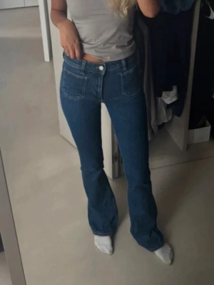Blå bootcut jeans med hög midja - Säljer ett par klassiska blå bootcut jeans med hög midja och framfickor. Jeansen har en snygg passform som sitter tajt över låren och släpper ut vid bensluten. Perfekta till vardagslooken och passar till det mesta. Materialet är denim i bomull.