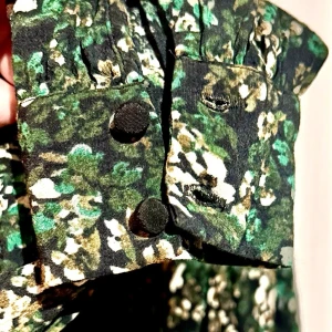 Blommig omlottblus från Vero Moda💚 - Säljer denna supersnygga mörkgröna omlottblus från Vero Moda i storlek S. Perfekt mönster med små söta blommor i grönt, vitt och svart. Modellen har ett jättefint draperat fall framtill, V-ringning och långa ärmar med superfina manschetter och klädda knappar! Materialet är 100% skön viskos (Lenzing EcoVero) som andas och sitter magiskt på. Skick: Helt oanvänd och i absolut nyskick! Mått (platt liggande): * Längd: ca 58cm * Byst: ca 36-37cm  * Ärmlängd: ca 61cm