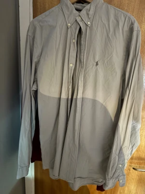 Ljusgrå skjorta från Polo Ralph Lauren - Klassisk ljusgrå skjorta från Polo Ralph Lauren i custom fit. Skjortan har button-down krage, långa ärmar och den ikoniska broderade loggan på bröstet. Tillverkad i mjuk bomull och stängs med vita knappar framtill.