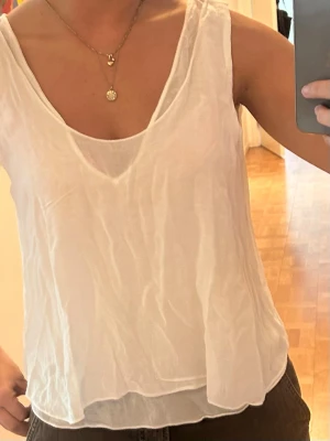Vit linnetopp med öppen rygg - Säljer en luftig vit linnetopp med v-ringning fram och djup öppen rygg. Toppen har ett tunt band över ryggen och knytning nedtill för en avslappnad look. Perfekt till varma dagar och enkel att styla med jeans eller kjol. Storlek M men passar även S.