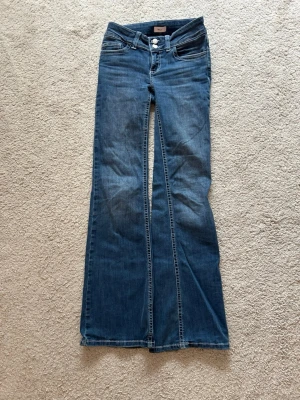 Blå bootcut jeans  - Snygga blå bootcut jeans med klassisk femficksdesign och broderade bakfickor. Jeansen har låg midja, dragkedja och knapp framtill samt kontrastsömmar. Det är använda typ 2 gånger.