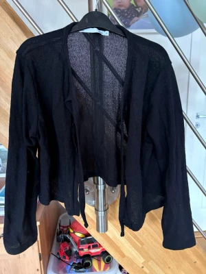 Svart tunn kofta från lager 157 - Svart, tunn och öppen kofta från 157 med långa ärmar. Koftan har ett lätt transparent material och knytband framtill. Perfekt att slänga över en topp för en chill look.