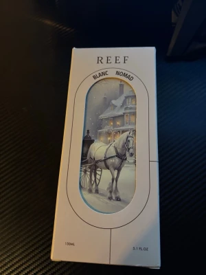 REEF Blanc Nomad parfym 150ml - Parfymen från det saudiska märket REEF. Blanc Nomad kommer i en elegant, genomskinlig glasflaska med ett vitt lock och detaljer i silver. Flaskan har ett vintrigt motiv med häst och släde framför ett hus. Förpackningen är vit med samma motiv och rymmer 150 ml. 