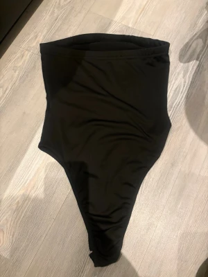 Svart body med hög midja - En stilren svart body med hög midja och klassisk skärning. Baddräkten har en enkel och tidlös design utan synliga detaljer eller mönster. 