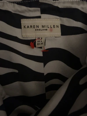 Zebramönstrad offshoulder topp Karen Millen - Säljer en snygg offshoulder topp från Karen Millen i svartvitt zebramönster. Toppen har en figurnära passform och är axelbandslös, vilket ger en trendig look. Perfekt för dig som vill stick sop ut med ett djurmönster.
